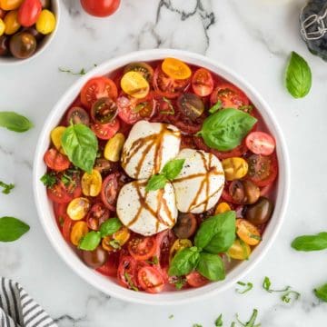 A Burrata Caprese Salad garnished with basil and drizzled with balsamic glaze.