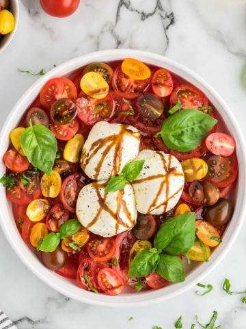 A Burrata Caprese Salad garnished with basil and drizzled with balsamic glaze.