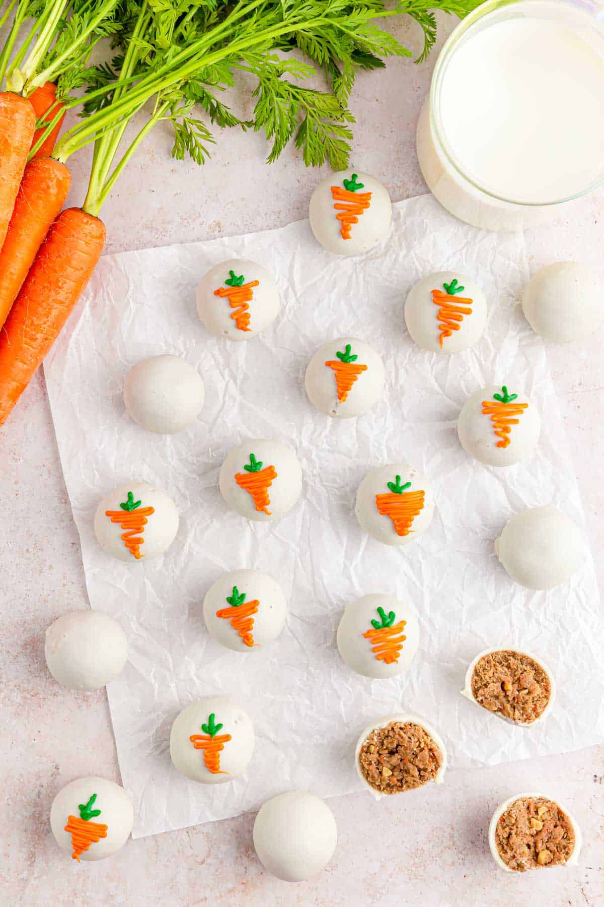 A table with carrot cake balls on parchment paper with some of the cake balls open to see the filled center.