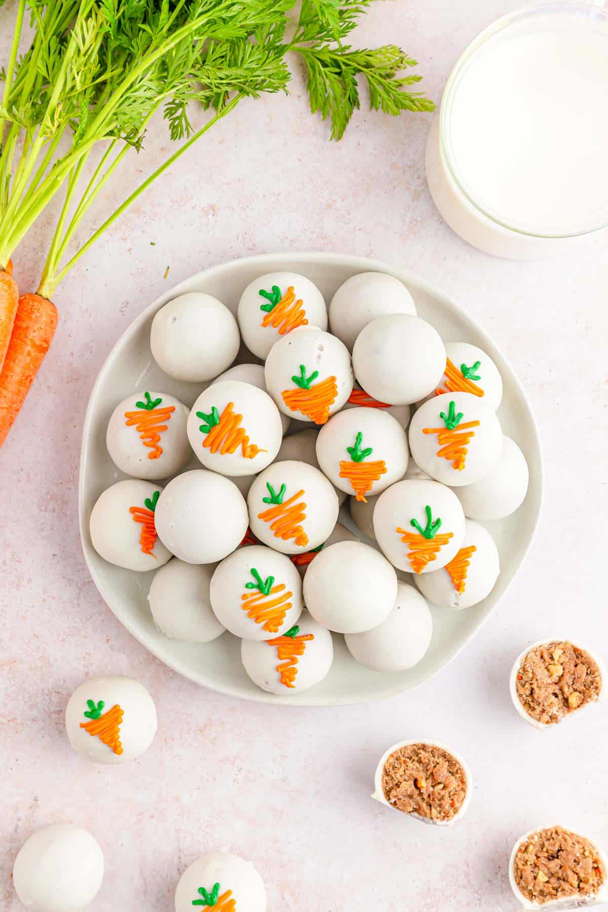 A white plate filled with carrot cake balls decorated with colored chocolate to look like carrots.