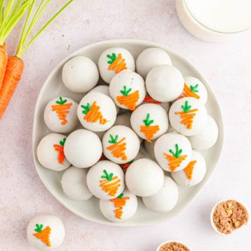 Overhead shot of a white plate filled with carrot cake balls and carrots and milk on the table for decor.