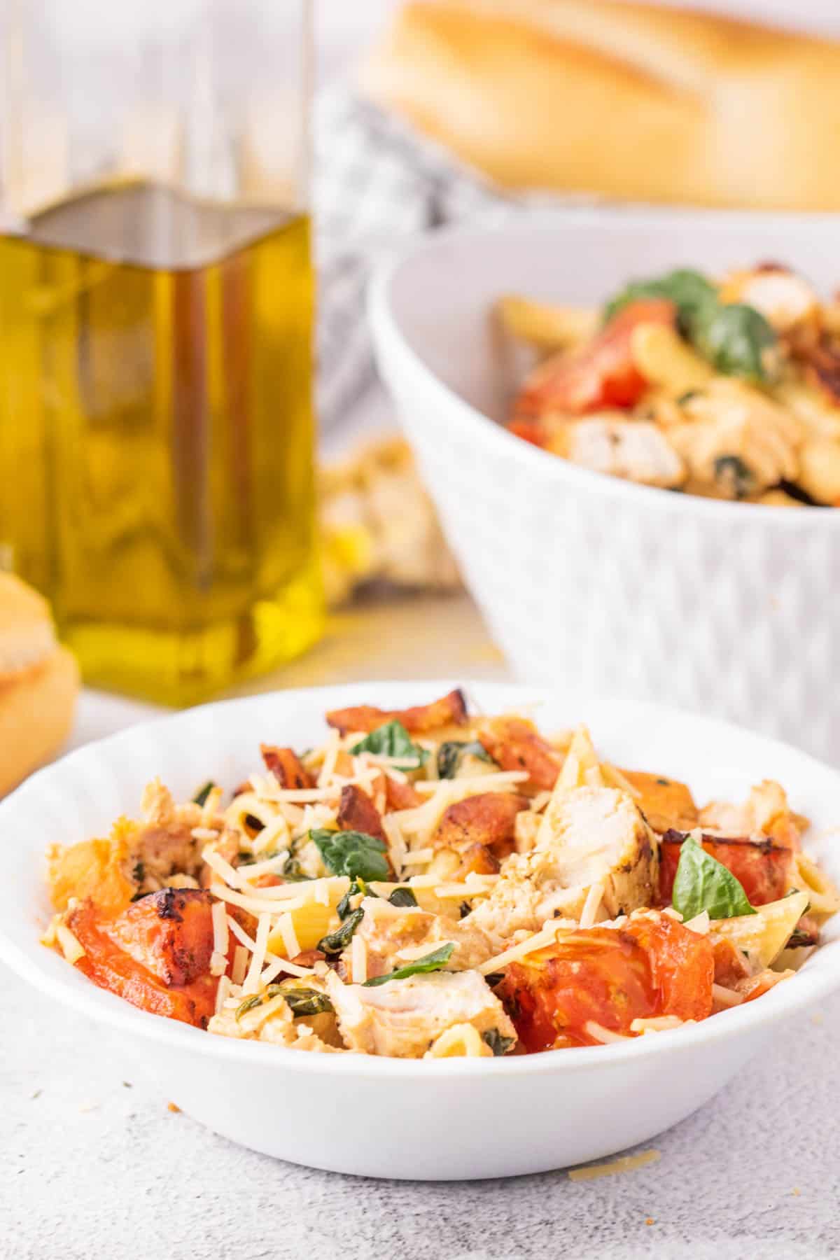 A white bowl filled with chicken and bacon pasta with spinach and tomatoes in a cream sauce.