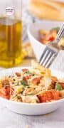This Chicken and Bacon Pasta with Spinach and Tomatoes recipe is featured in a white bowl with a fork picking up a delicious bite.