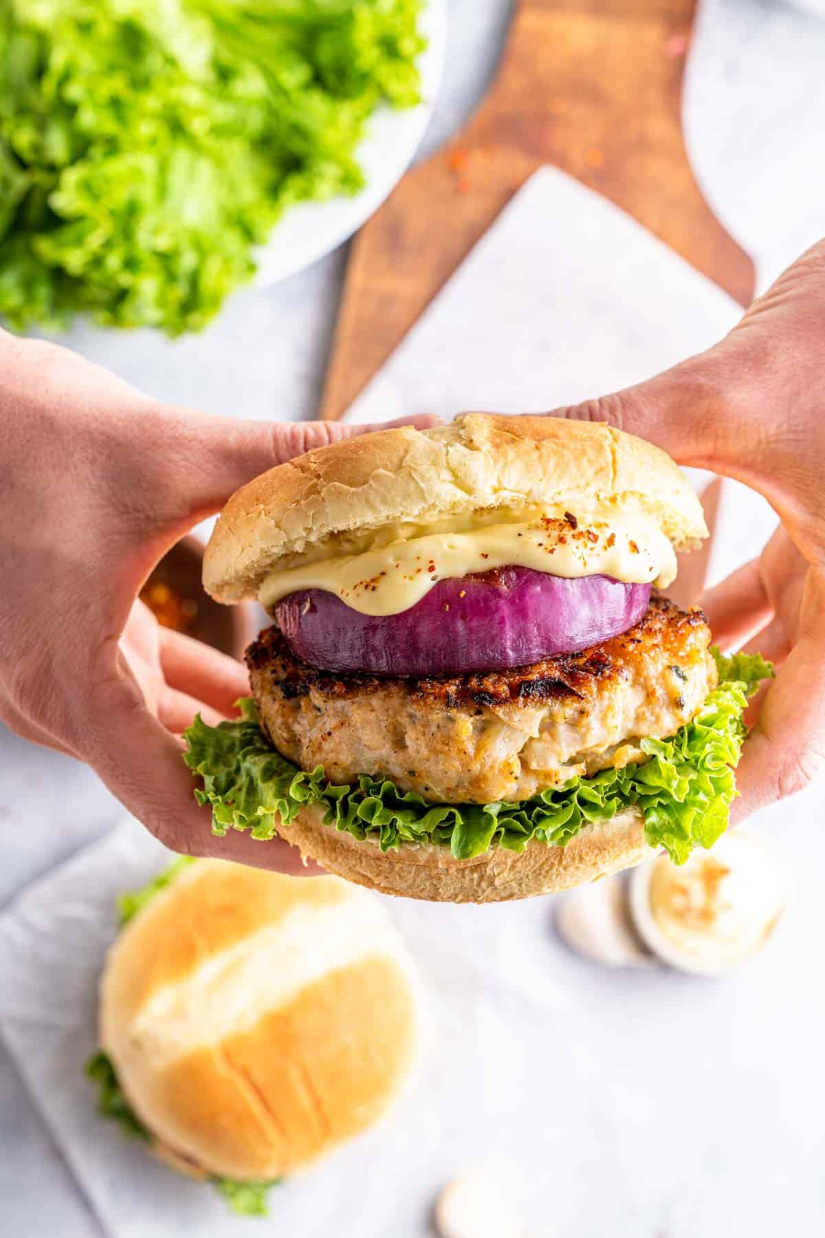 Two hands holding a chicken burger with burger sauce.