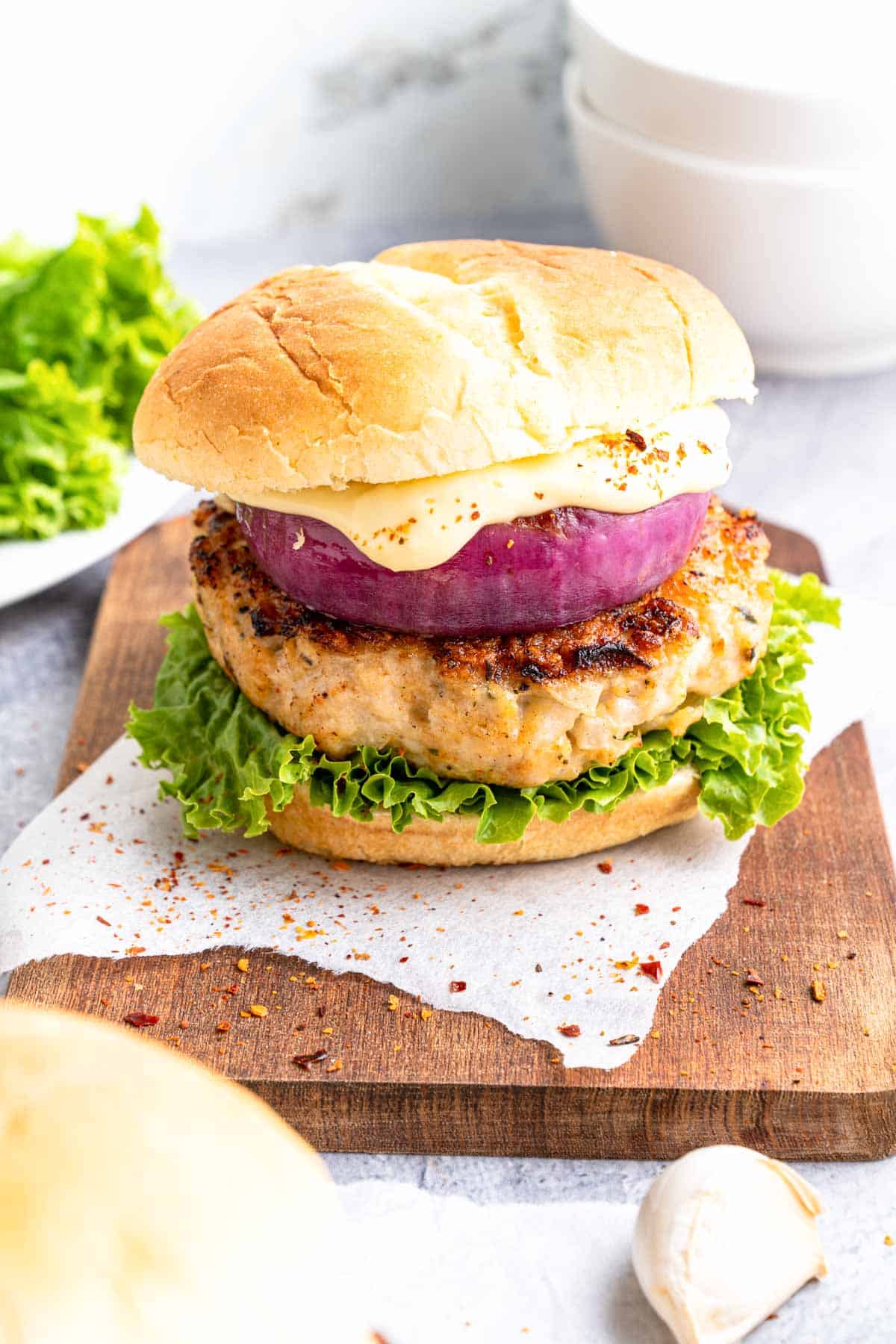 A chicken burger on a bun with lettuce, red onion, and sauce.