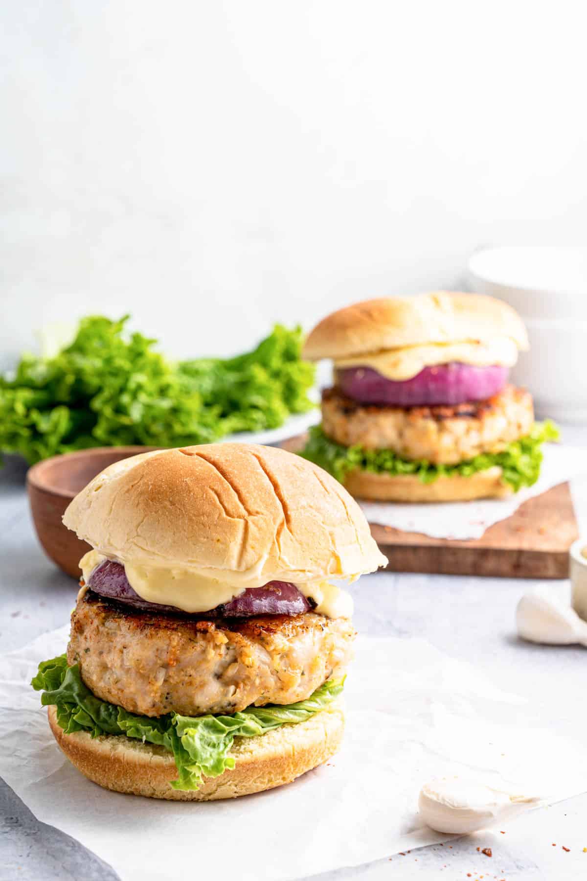 Two ground chicken burgers set on a table with lettuce in the background.