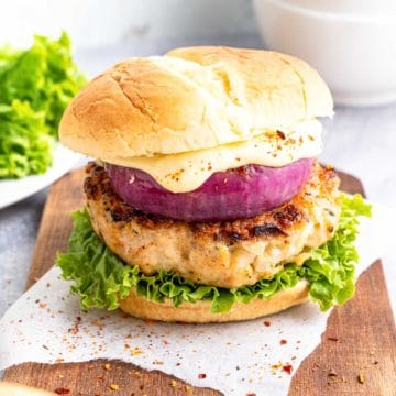 A chicken burger on a bun with lettuce, red onion, and sauce.