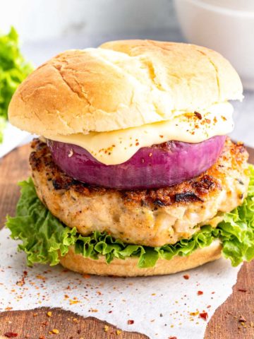 A chicken burger on a bun with lettuce, red onion, and sauce.