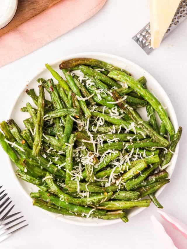 Air fryer green beans on a white plate garnished with fresh parmesan cheese.