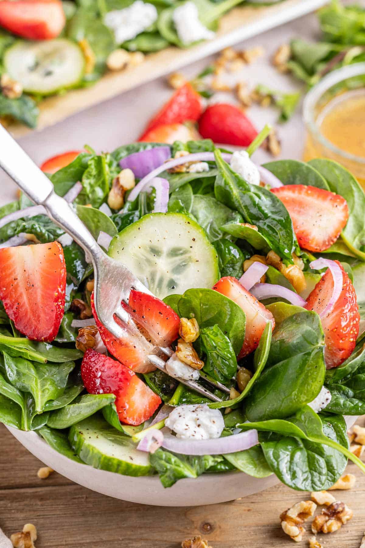 A fork with a bite of salad and strawberry, cheese, and walnut.