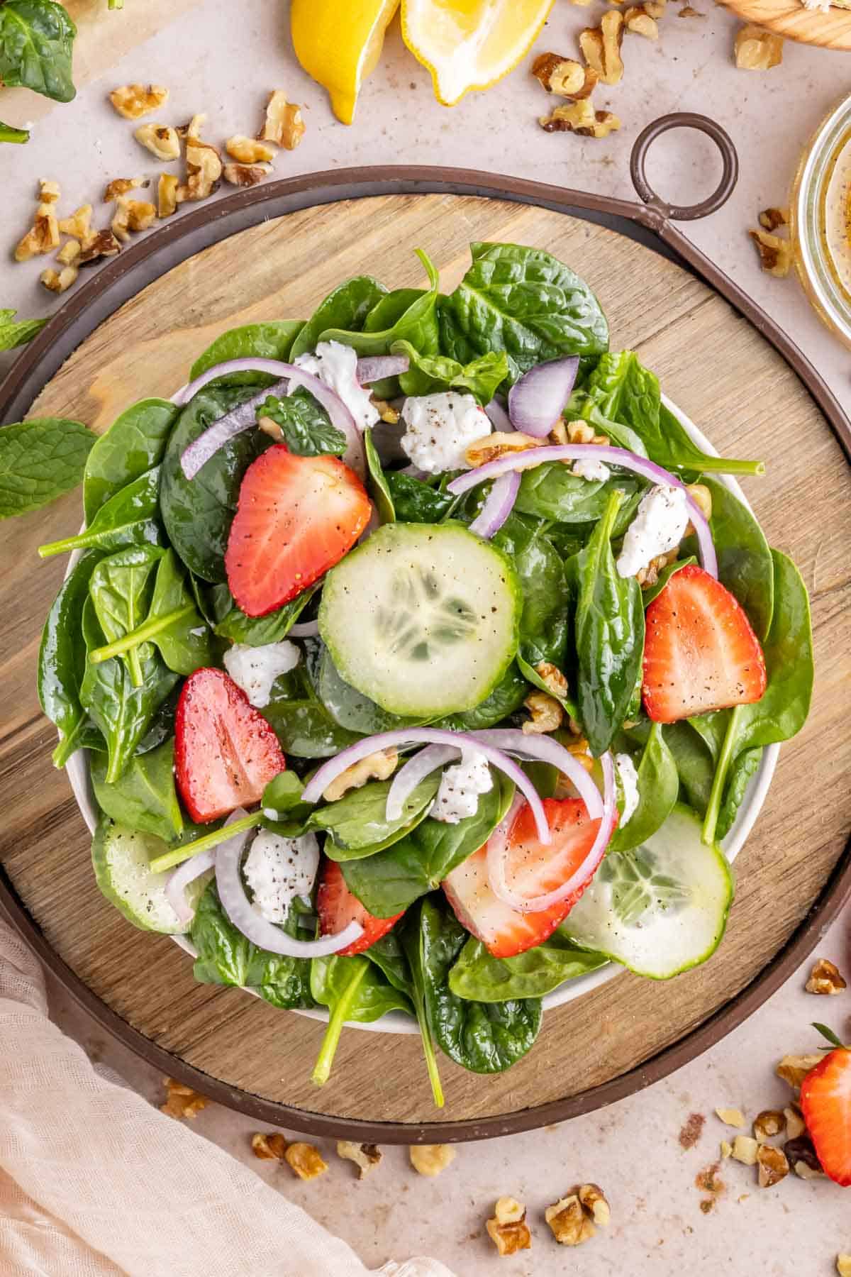 A bowl of strawberry salad with goat cheese in a white bowl on a wooden tray.