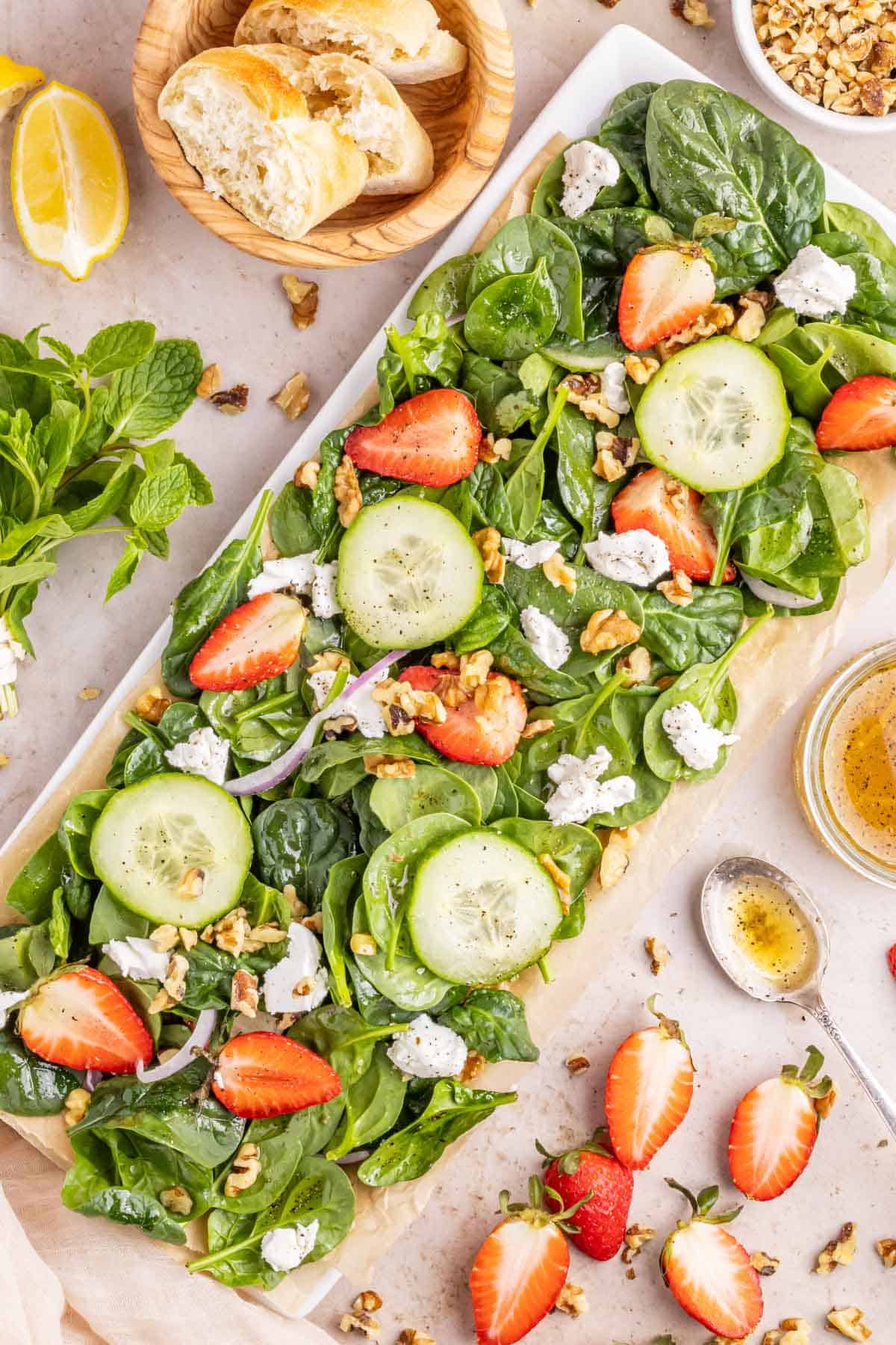 A white rectangular serving plate with a strawberry spinach salad with lemon vinaigrette.