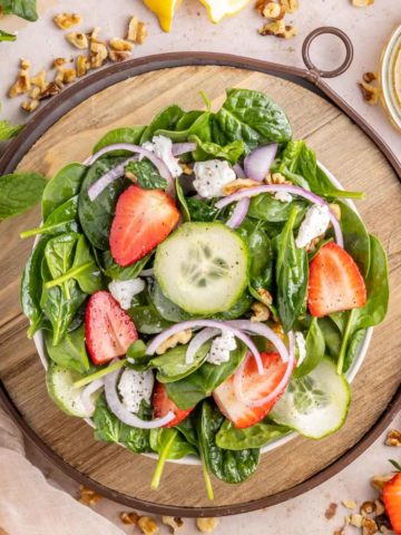 A bowl of strawberry spinach salad with lemon vinaigrette in a white bowl set on a wooden tray.