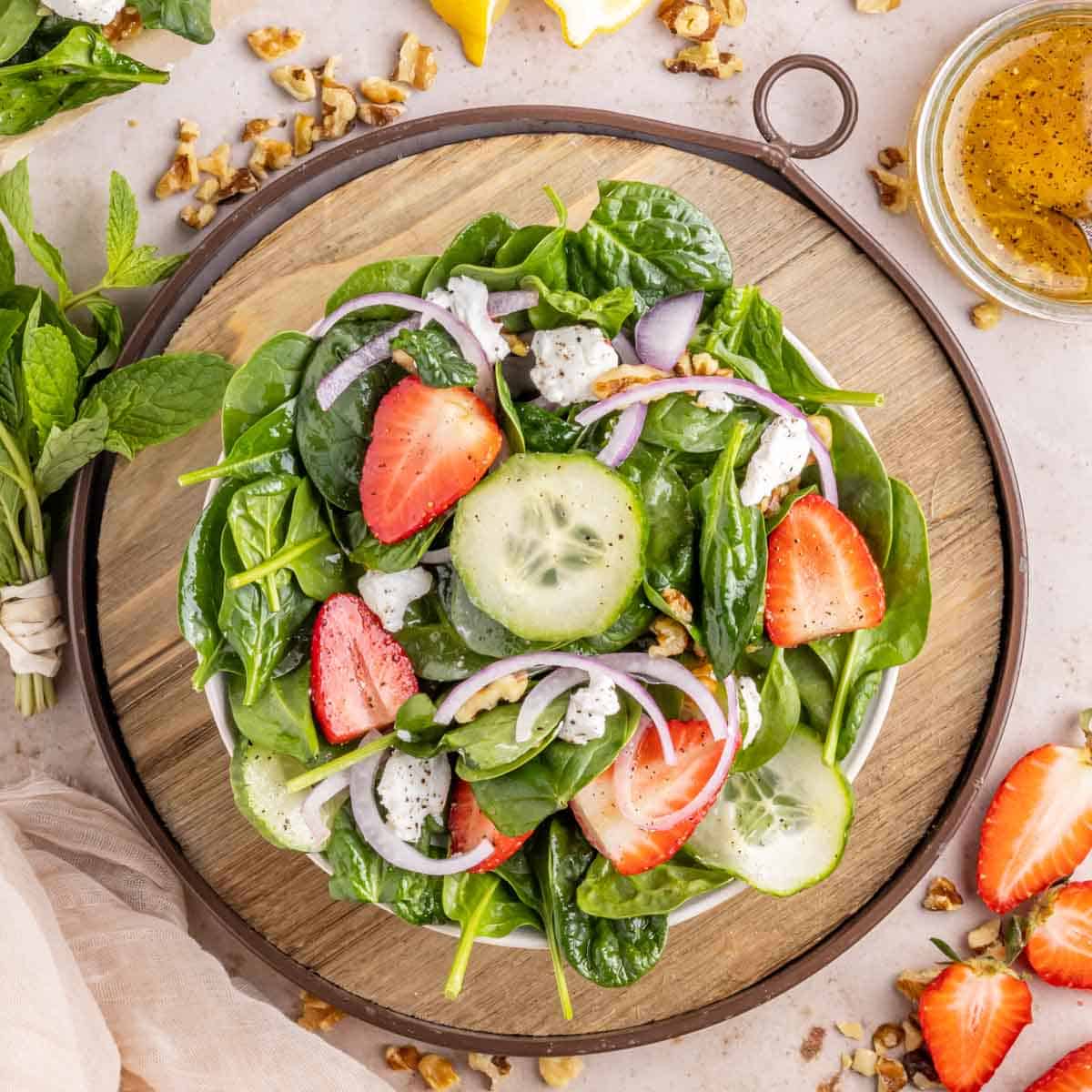 A bowl of strawberry spinach salad with lemon vinaigrette in a white bowl set on a wooden tray.