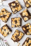 Smores brownies spread out on a table and topped with marshmallows.