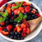 Berry Fruit Salad tossed in a honey lime dressing in a rustic bowl with some of the berries being scooped out with a wooden spoon.