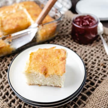 A slice of a butter swim biscuit on a white plate with the pan of biscuits in the background.