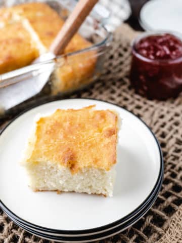 A slice of a butter swim biscuit on a white plate with the pan of biscuits in the background.