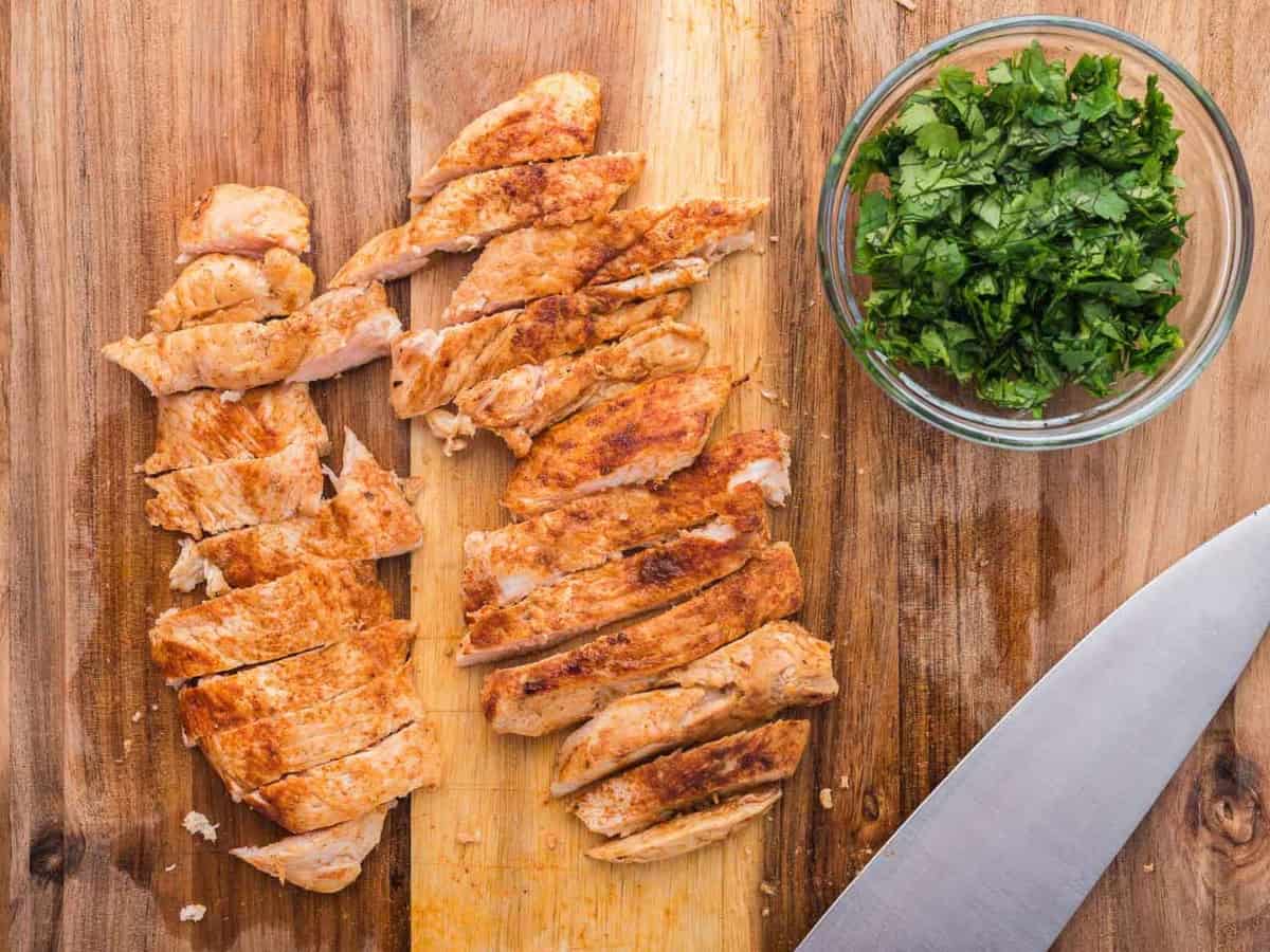 Sliced seasoned chicken on a wooden cutting board.