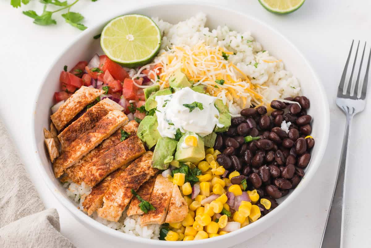 A white bowl filled with all the ingredients needed to assemble a chicken burrito bowl.