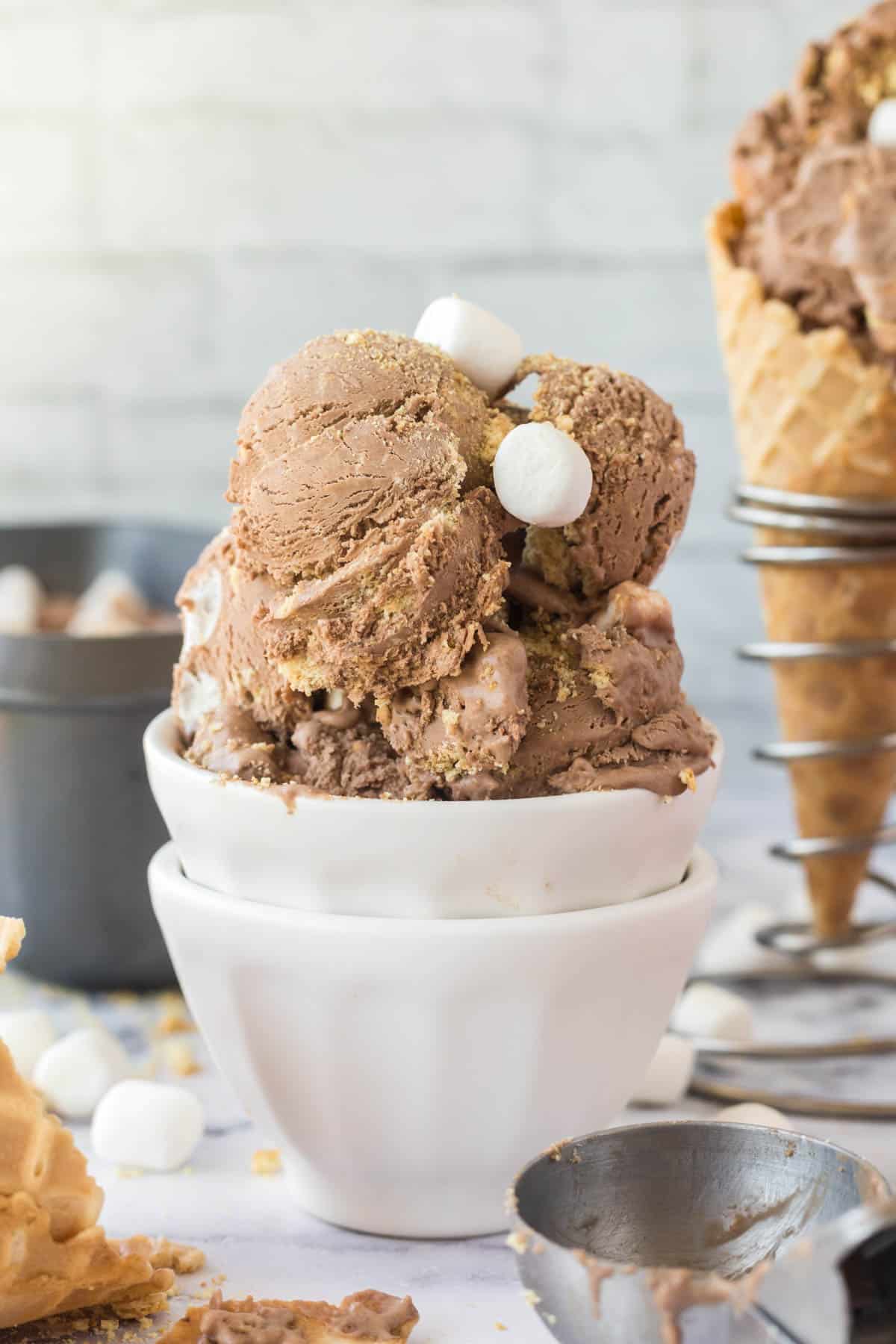 S'mores Ice cream in a white dish with some of the ice cream in a waffle cone in the background.