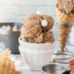 S'mores Ice cream in a white dish with some of the ice cream in a waffle cone in the background.