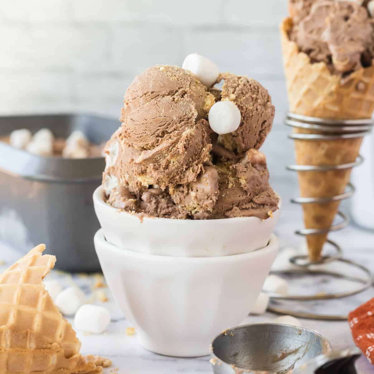 S'mores Ice cream in a white dish with some of the ice cream in a waffle cone in the background.