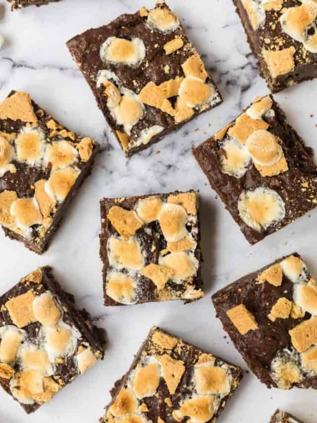 Smores brownies spread out on a table and topped with marshmallows.