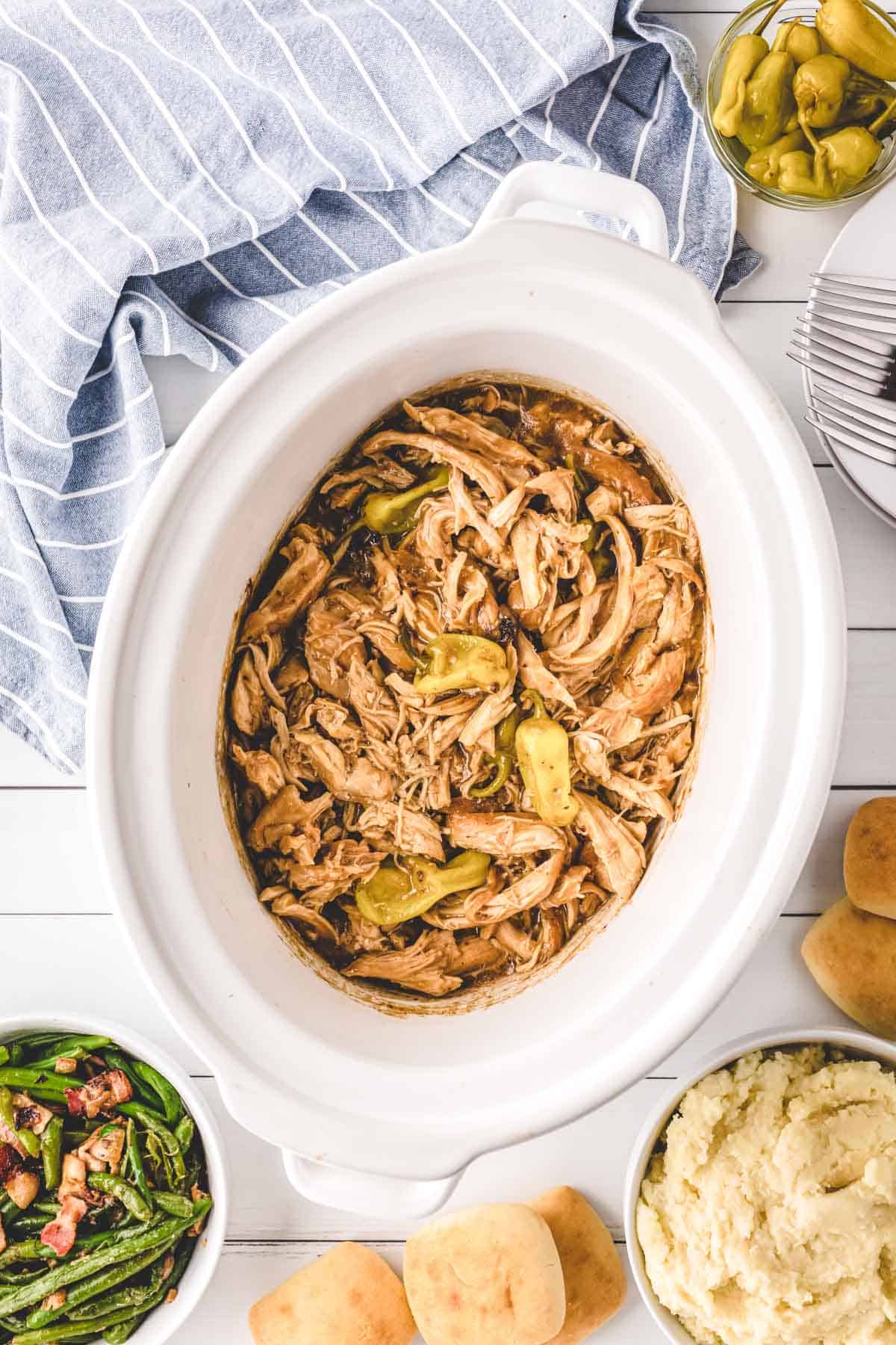 A white slow cooker filled with Mississippi Chicken.