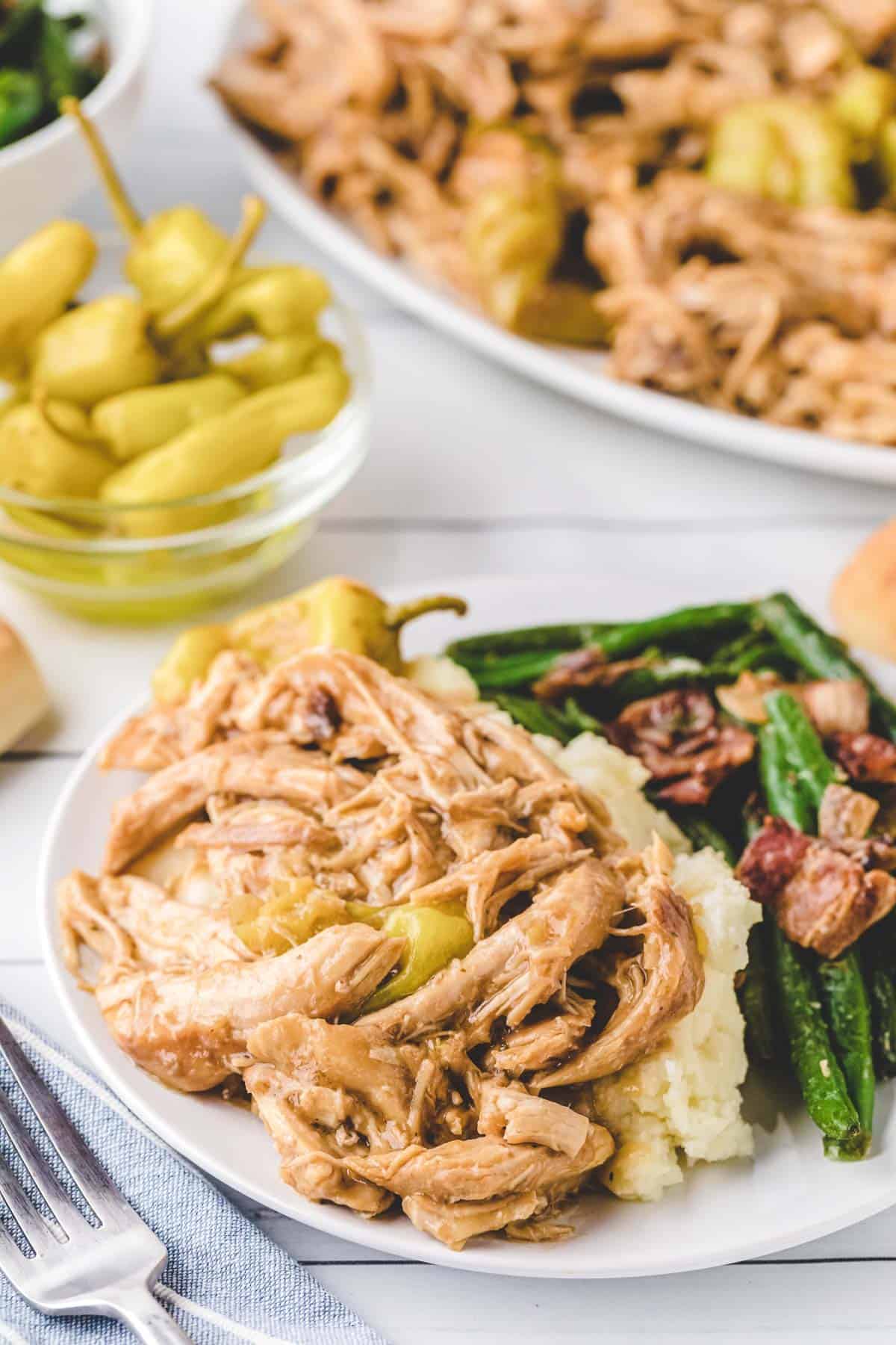 A plate of Mississippi Chicken served over mashed potatoes with green beans.