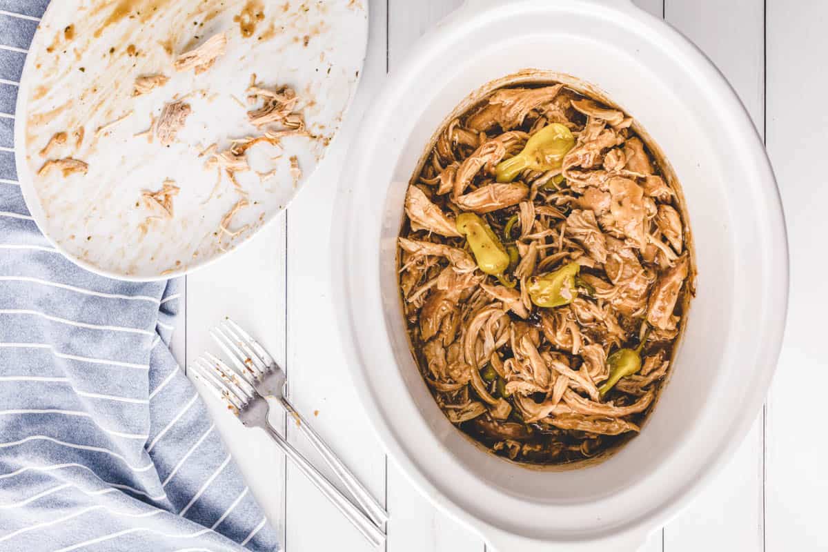 A white crock pot filled with shredded Mississippi chicken.