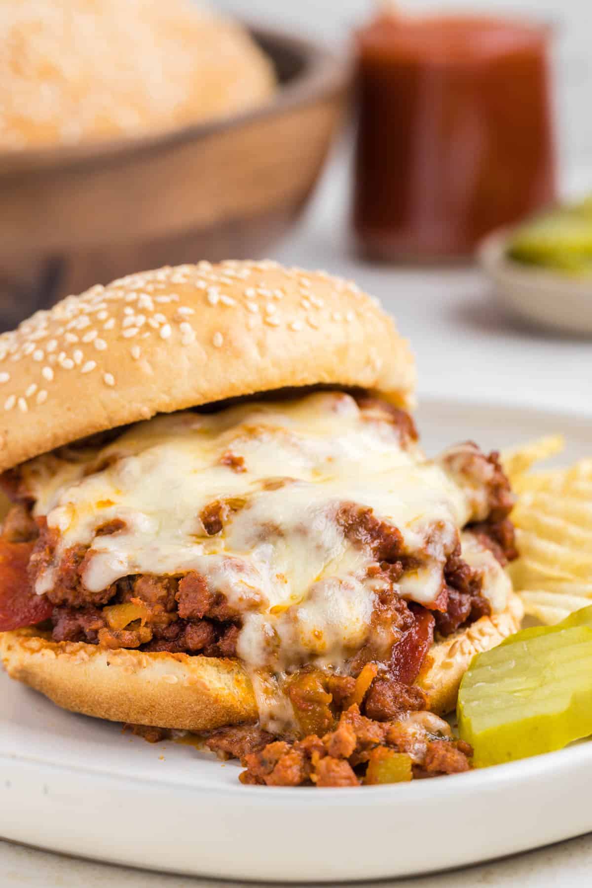 Pizza Sloppy Joe sandwich on a gray plate served with a pickle slice and chips.