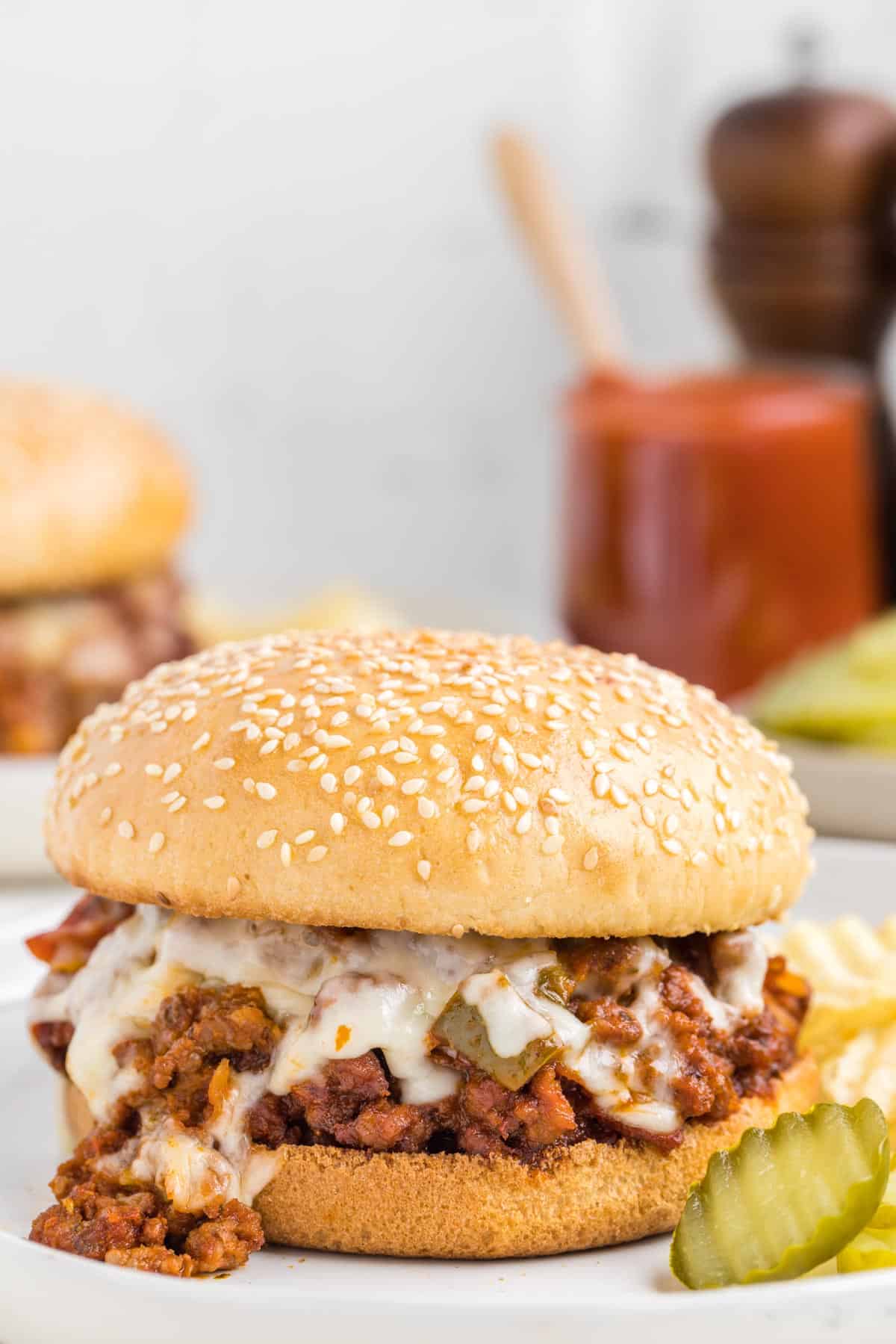 A pizza sloppy joe with melted mozzarella on a toasted sesame seed bun with extra pizza sauce in the background.