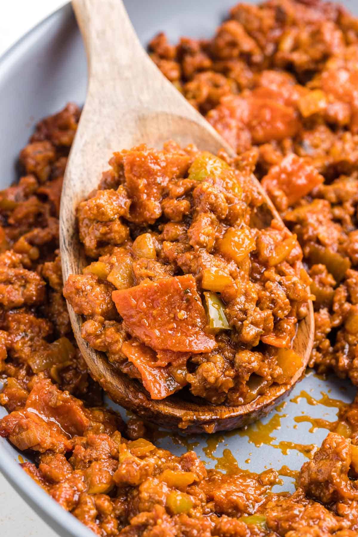 A skillet of pizza sloppy joes with a wooden spoon removing a scoop.