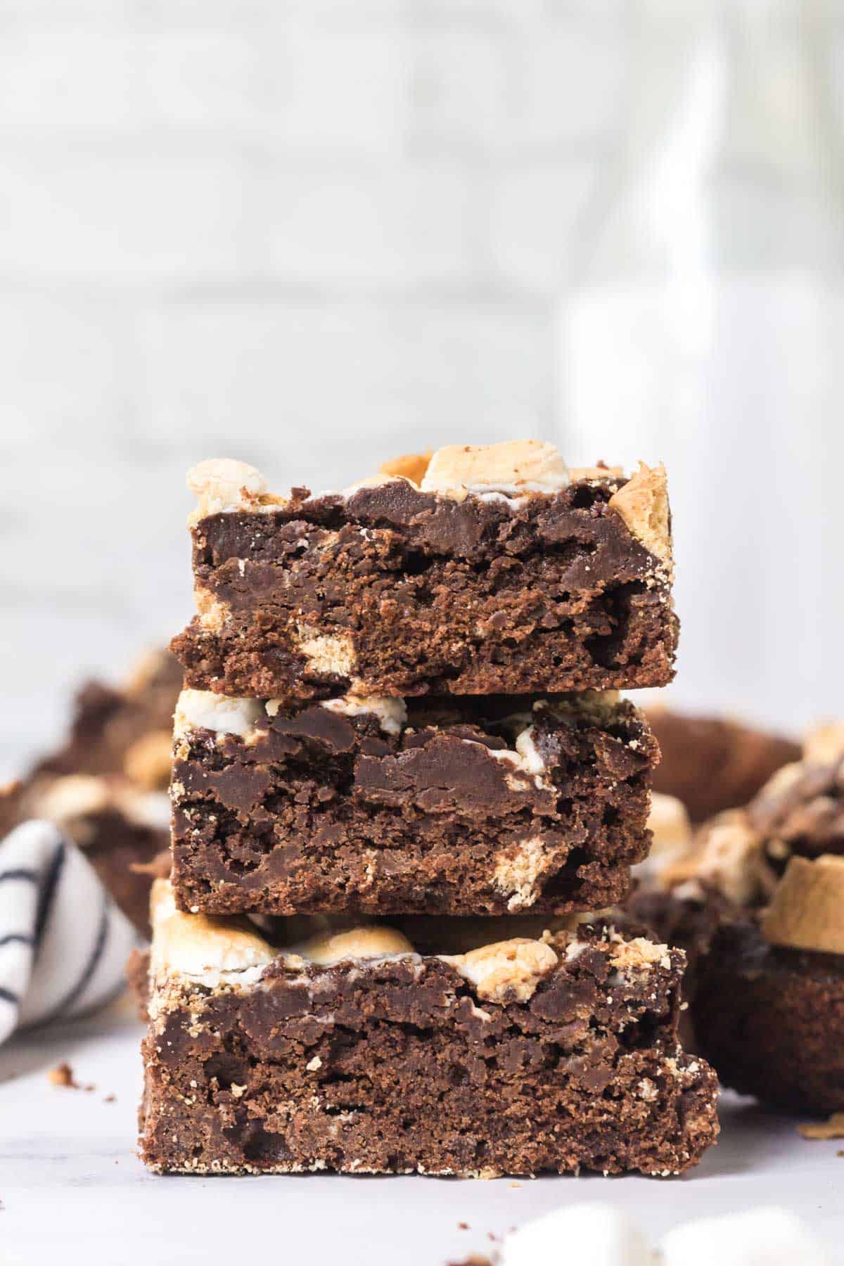 A stack three high of s'mores brownies on a white marble table with a milk jug in the background.