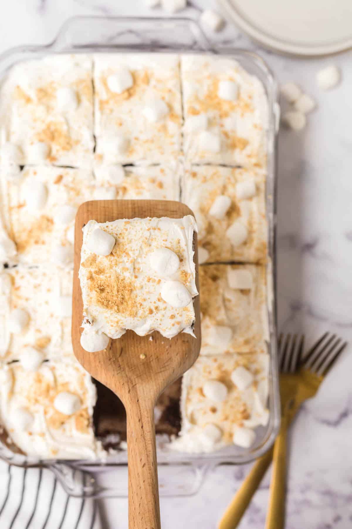 A wooden spatula holding a piece of easy s'mores cake recipe that was removed from the cake pan.