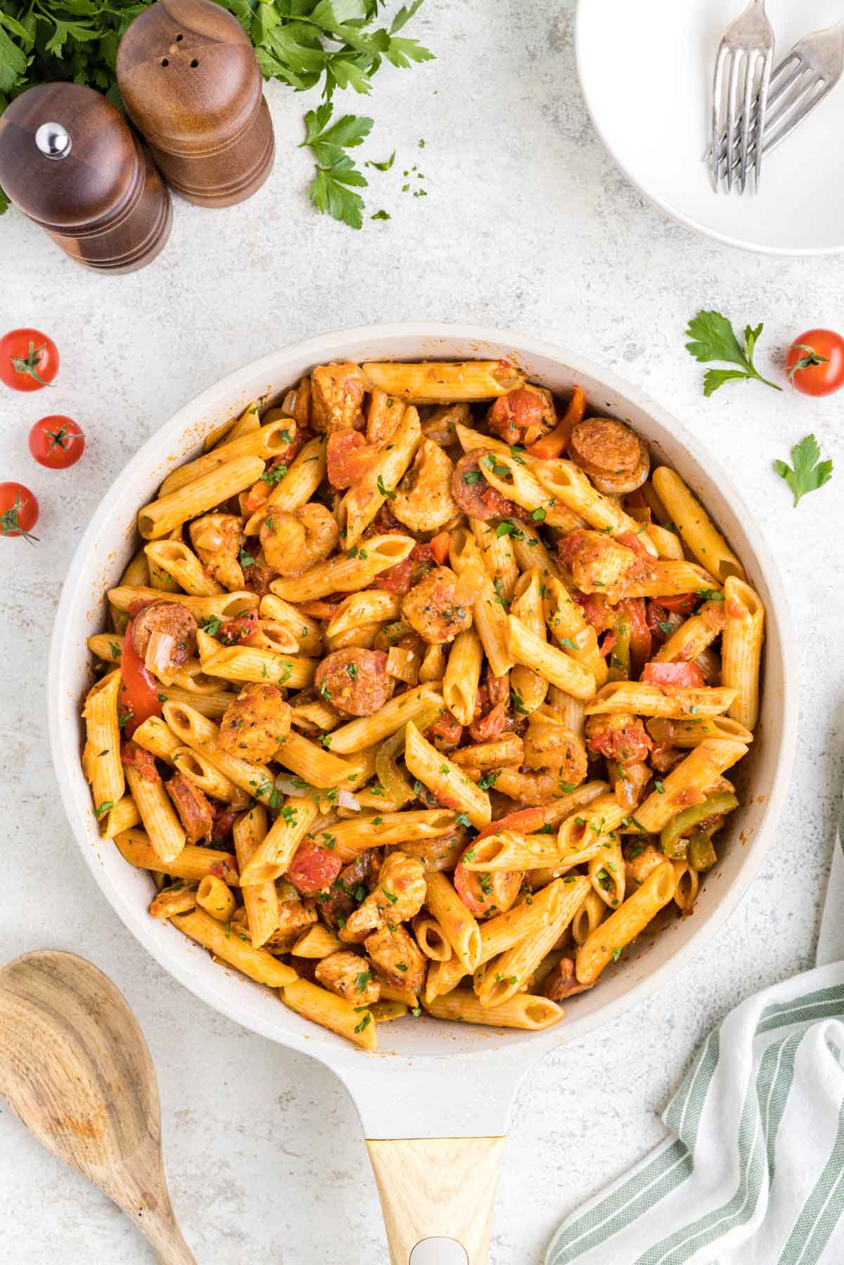 A skillet filled with cajun jambalaya pasta set on a white table with salt & pepper shakers in the background.