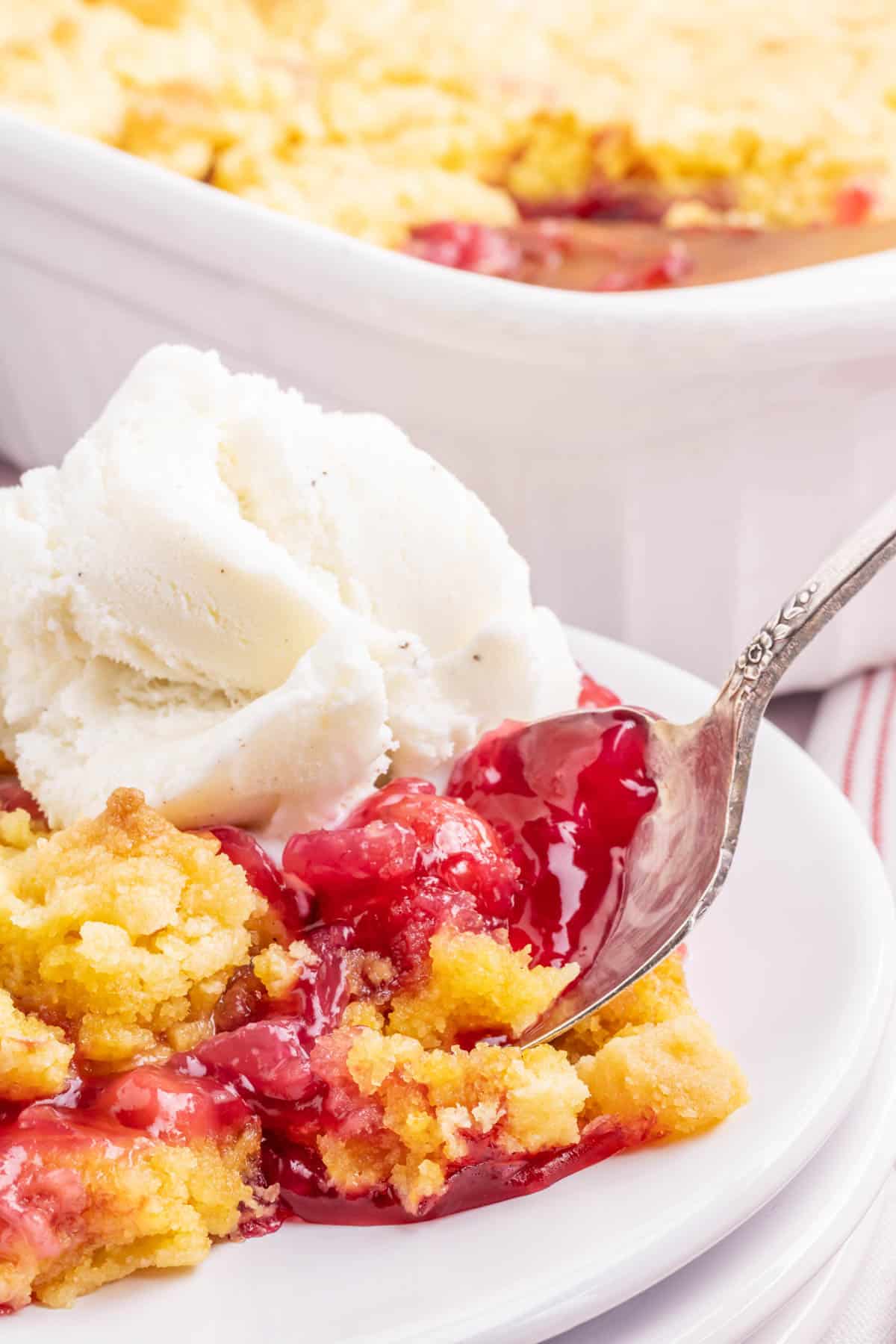 A plate of cherry pineapple dump cake on a plate with a spoon removing a bite.