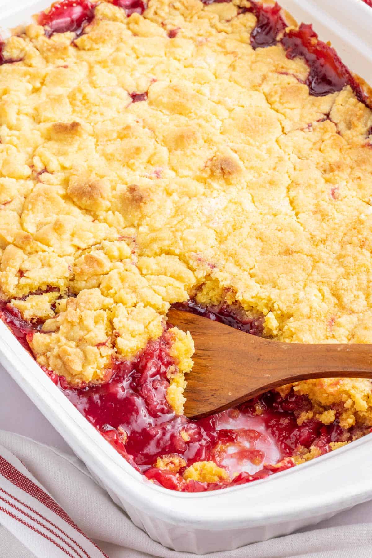 A white baking dish filled with cherry pineapple dump cake with a spoonful removed.