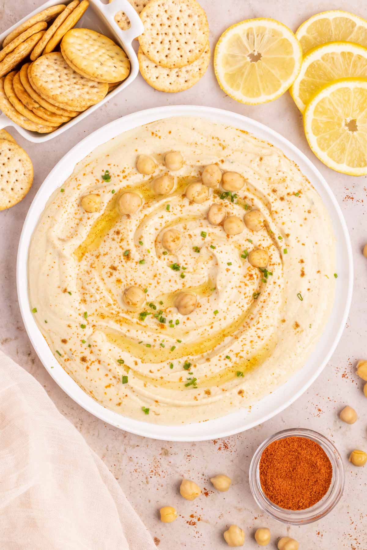 A bowl of creamy garlic hummus garnished with olive oil, red pepper, and chickpeas.