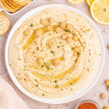 A bowl of creamy garlic hummus garnished with olive oil, red pepper, and chickpeas.