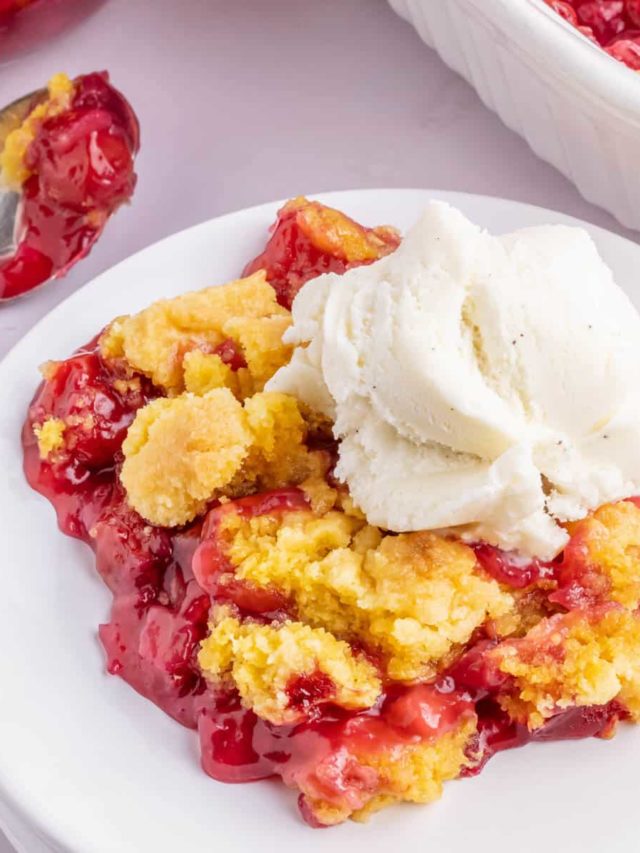 A white plate filled with a serving of cherry pineapple dump cake topped with a scoop of vanilla ice cream.