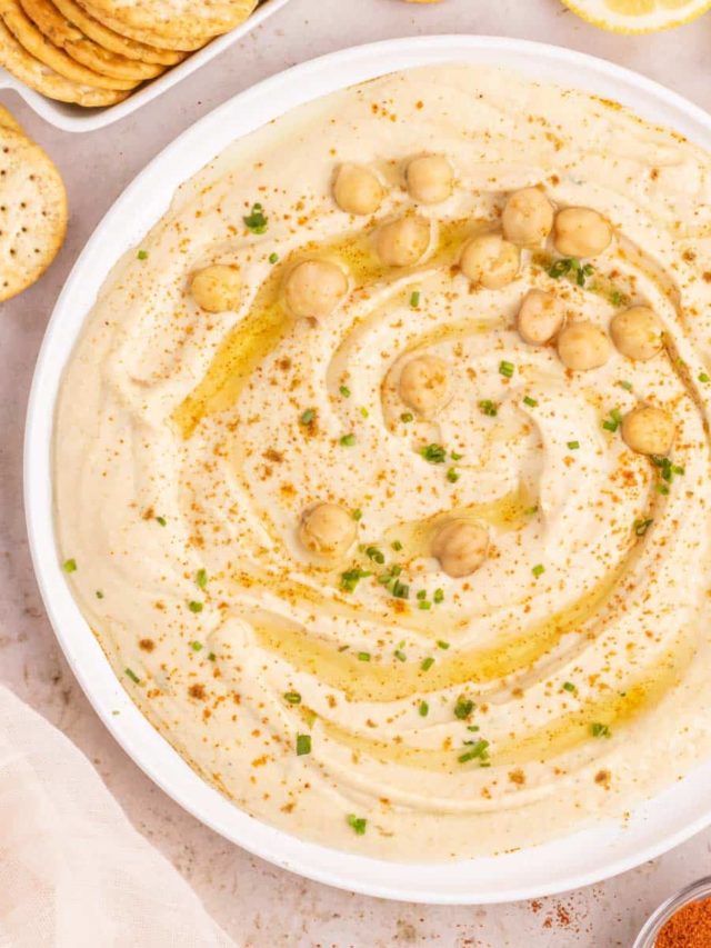A bowl of creamy garlic hummus garnished with olive oil, red pepper, and chickpeas.