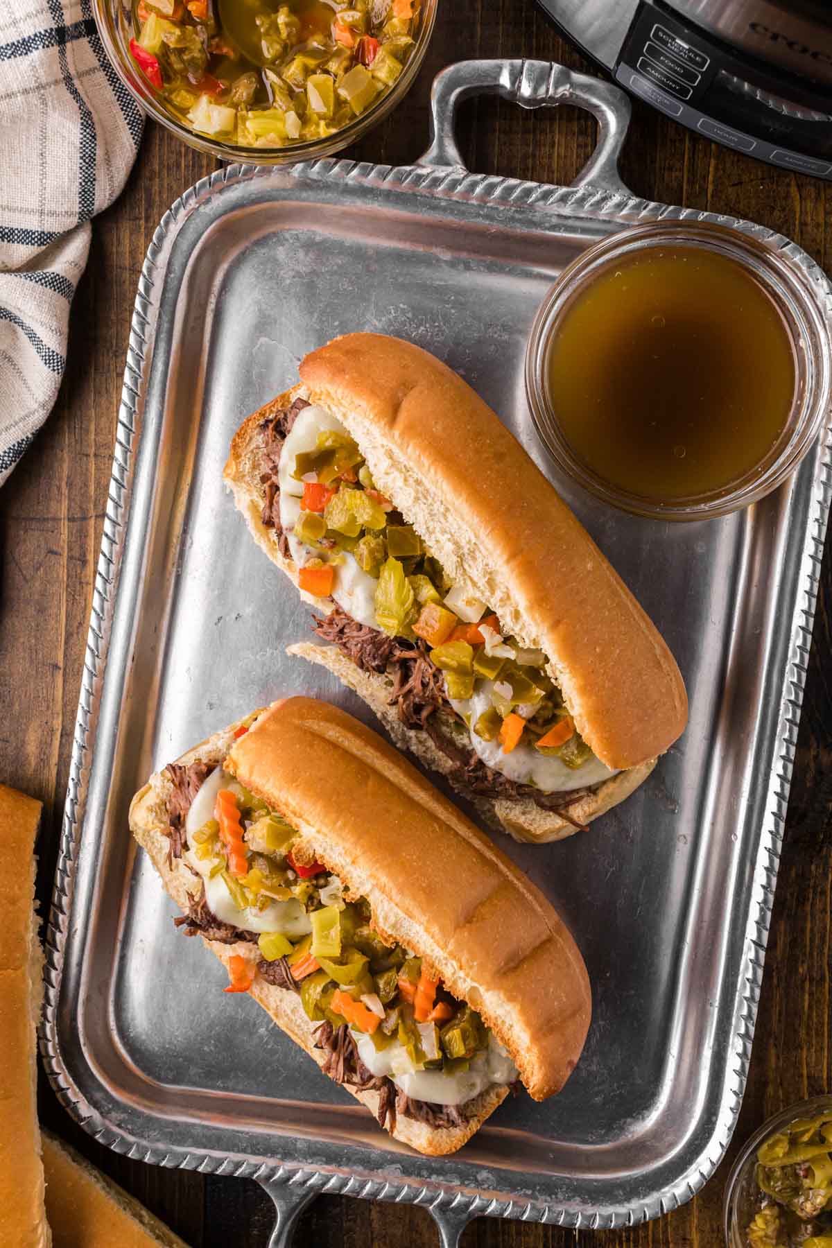 A silver serving tray with two Italian beef sandwiches and a bowl of au-jus.