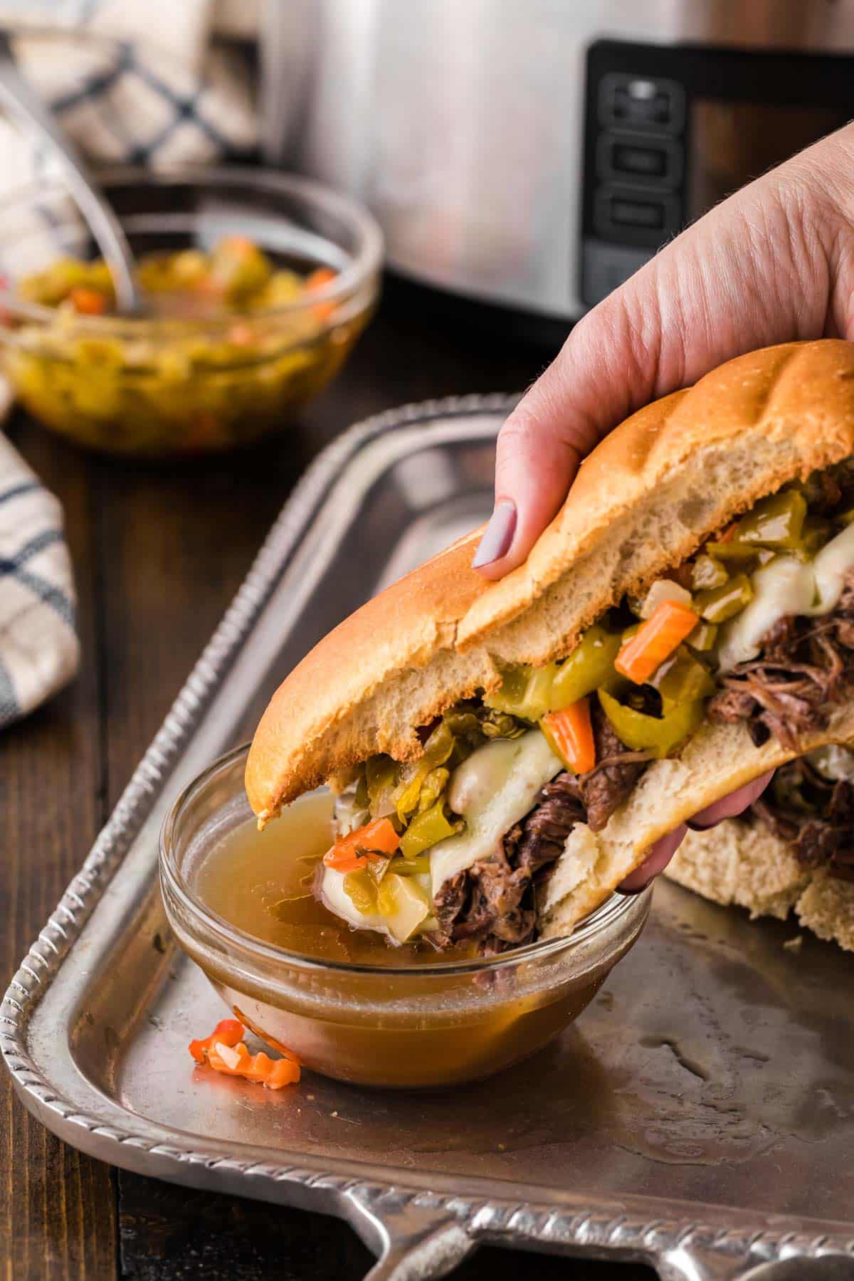 An Italian Beef sandwich being dipped in a bowl of au-jus.