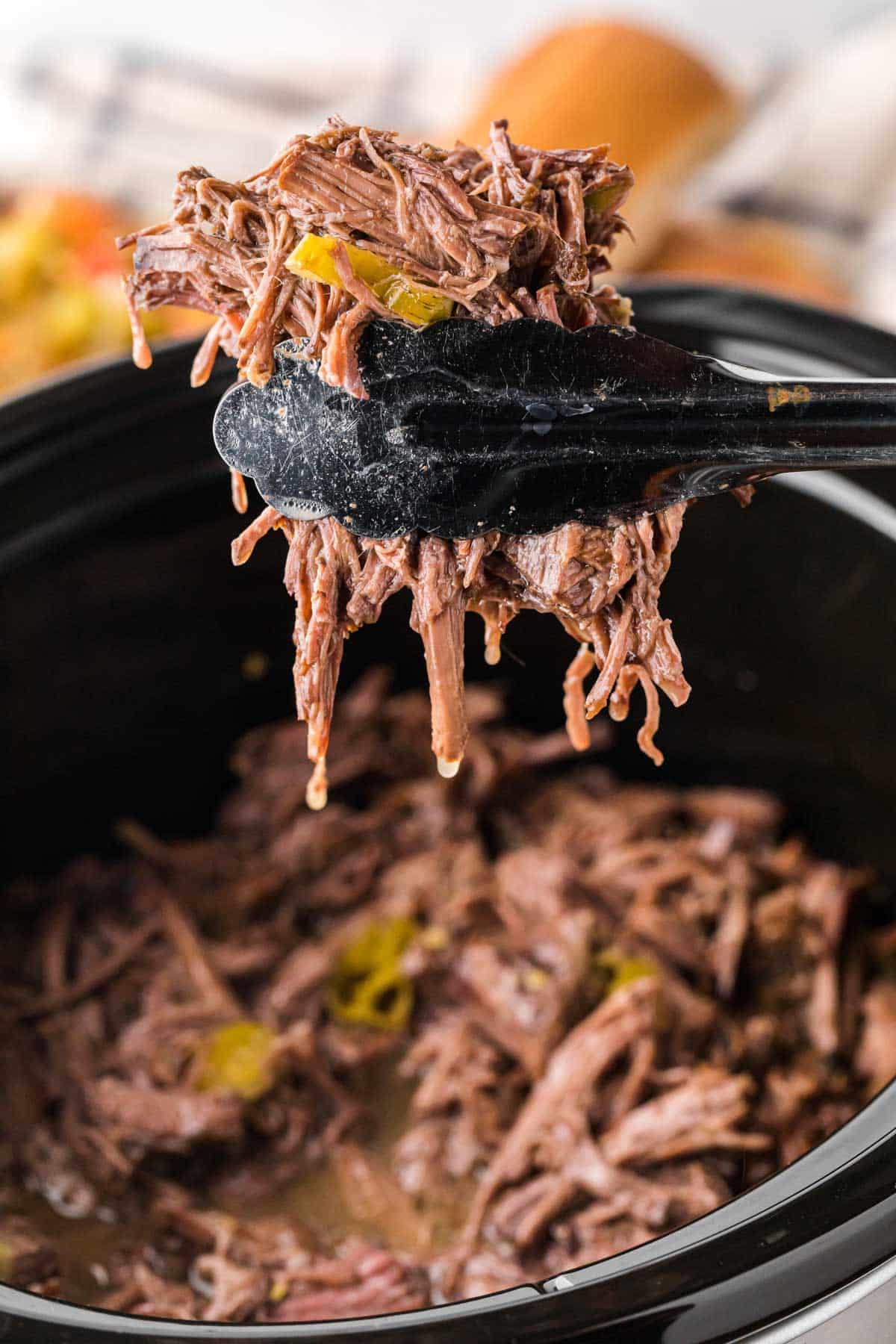 Tongs removing beef from the slow cooker.