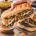 An Italian Beef sandwich being dipped in a bowl of au-jus.