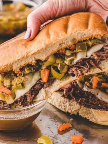 An Italian Beef sandwich being dipped in a bowl of au-jus.