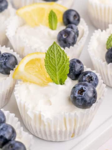 A tray of no-bake mini lemon cheesecakes garnished with lemon slice, blueberries and mint.