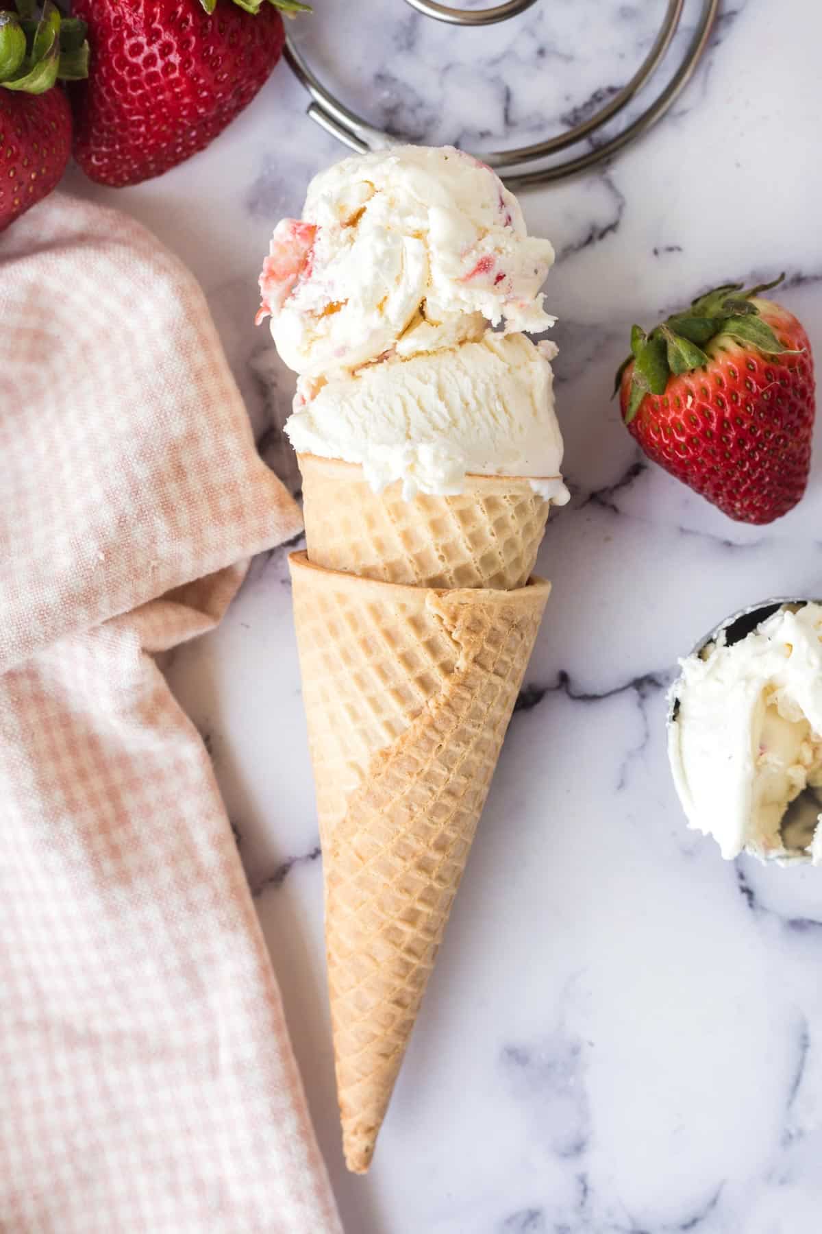 A waffle cone filled with two scoops of strawberry ice cream.